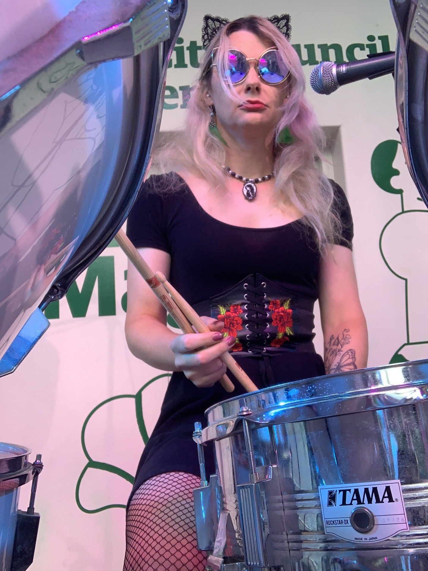 Siân Feehan drums while wearing large reflective glasses, a black outfit and fishnets.