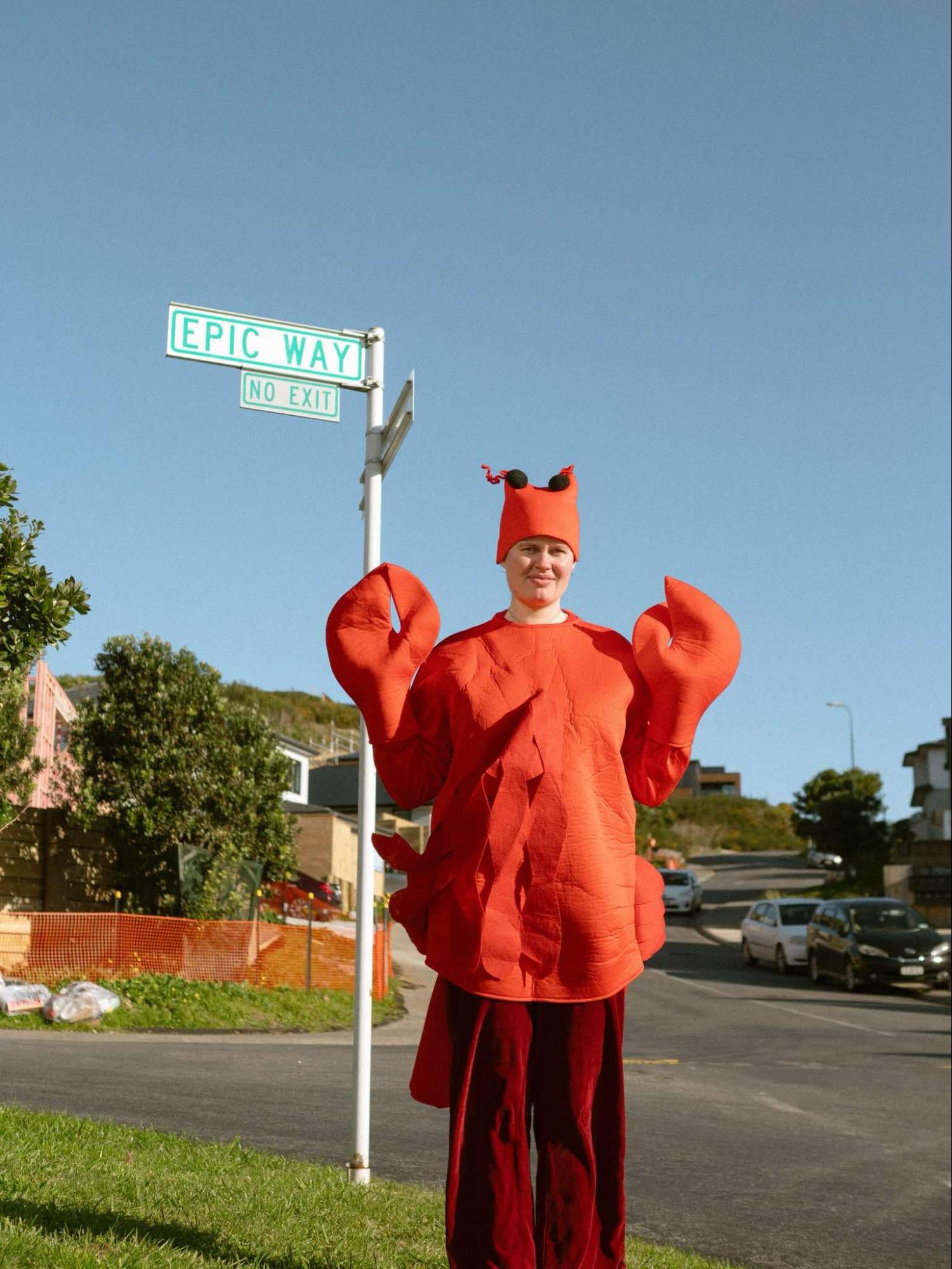 Liv Ward dressed in a bright orange lobster suit next to a street sign ‘Epic Way’.